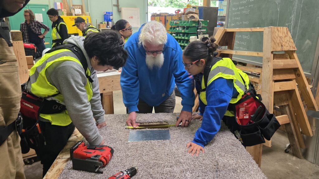 two students watch an instructor measure a hole in a work area to replicate a duct vent