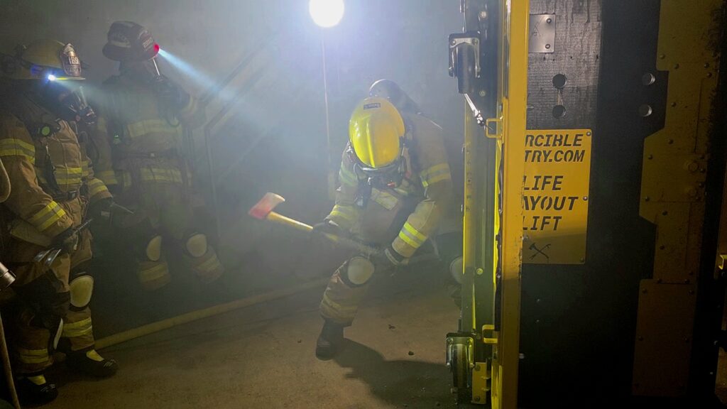 A firefighter swings his ax to break the hinges on a door prop