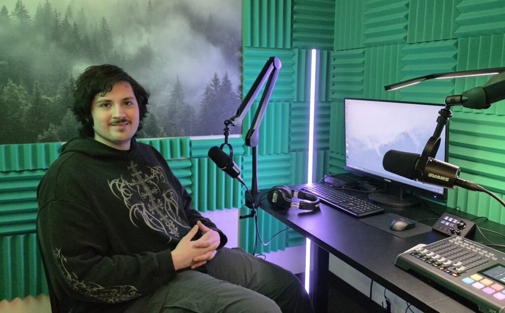 Ezra Haines sits in the Audio Lab with the sound booth equipment