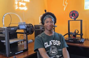 Maleek Moore sitting in the Prototype Lab room with 3D printers in the background