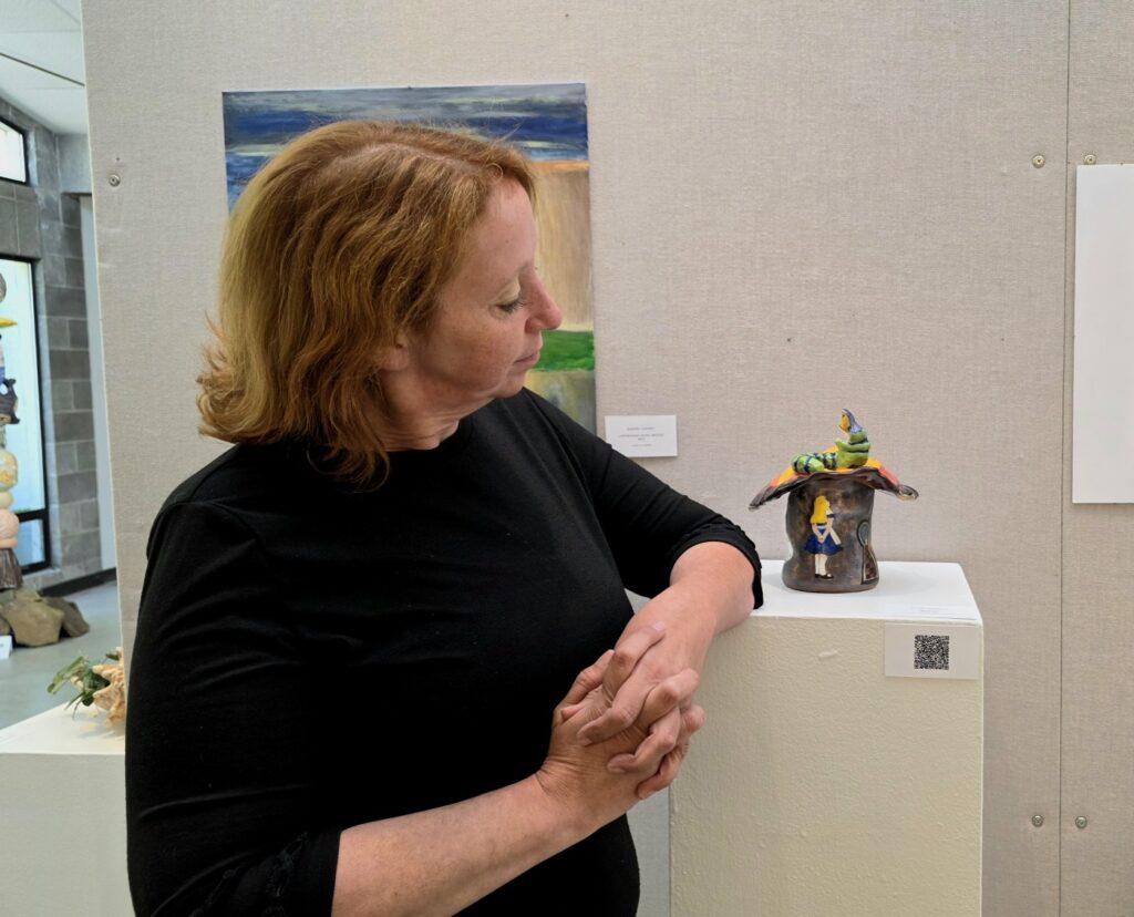Naomi Roberts stands next to her sculpture she created with Alice in Wonderland figures on it