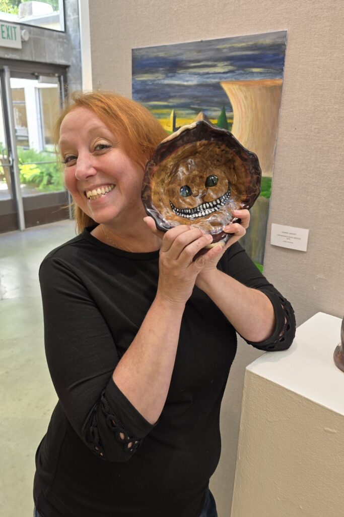 Naomi Roberts holds a piece of ceramic art she created that features the Cheshire cat from Alice in Wonderland.