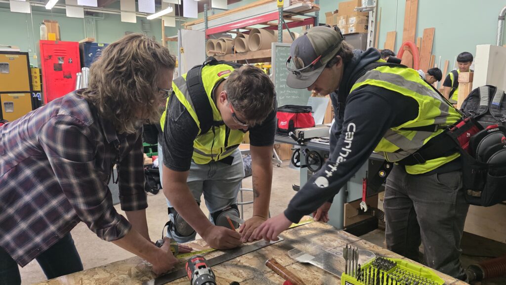 Students working with tools to cut a vent duct hole during a workshop